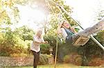 Grandmother pushing granddaughter on swing in backyard