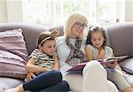 Grandmother and granddaughters reading book on living room sofa