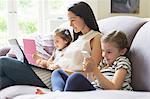 Mother and daughters with laptop, cell phone and digital tablet on sofa