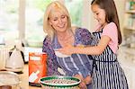 Grandmother and granddaughter baking sifting flour in kitchen