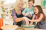 Playful grandmother and granddaughters sprinkling flour in kitchen