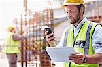 Construction worker with digital tablet texting with cell phone at construction site
