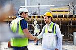 Construction worker and engineer with blueprints handshaking at construction site