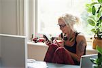 Young woman with headphones and tattoo texting in home office