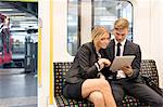 Businessman and businesswoman sharing digital tablet, London Underground, UK