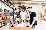 Friends standing around workbench in carpentry workshop talking