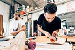 Young man in carpentry workshop attaching wheels to skateboard