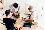 High angle view of young men standing around workbench attaching wheels to skateboards