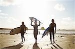 Three female friends on beach, holding surfboards