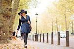 Stylish young woman strolling through autumn leaves in city park