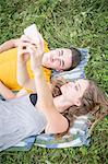 Young couple lying on grass in field, taking self portrait using smartphone