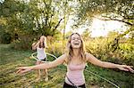 Two young girls in rural environment, fooling around, using hula hoops,