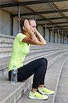 Young female runner adjusting headphones from stadium seating