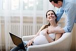 Pregnant woman sitting in chair, using laptop, husband holding her hand