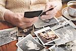 Senior woman sitting at table, looking through old photographs, mid section
