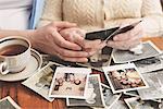 Senior woman and granddaughter sitting at table, looking through old photographs, mid section