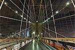 Brooklyn bridge walkway and distant Manhattan financial district skyline at night, New York, USA