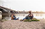 Four friends sitting on riverbank, Warsaw, Poland