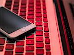 High angle view of cellular phone on computer keyboard in red lighting