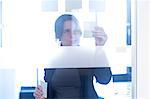 Businesswoman sticking notes on glass wall in office