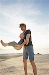 Mature man swinging his toddler daughter on beach, Calvi, Corsica, France