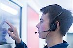 Side view of young man wearing headset using touch screen computer monitor