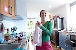 Mid adult woman in kitchen drying hands on tea towel looking away smiling