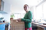 Low angle view of mid adult woman in kitchen holding basket looking at camera smiling