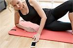 Cropped view of mature woman lying on side on yoga mat looking down using smartphone