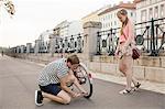 Young woman watching young man kneeling inflating bicycle tyre