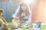 Girl having teddy bear picnic in garden holding toy teacup