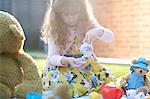 Girl having teddy bear picnic in garden pouring tea