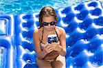 Teenager using smartphone on inflatable in swimming pool