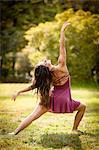 Full length rear view of mid adult woman wearing short dress dancing on grass, head back arm raised