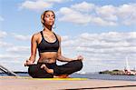 Young woman sitting cross legged by water in yoga position, eyes closed, Philadelphia, Pennsylvania, USA