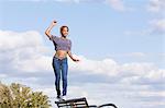 Young woman wearing crop top balancing on back on park bench