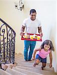 Father and daughter walking up stairs carrying breakfast on tray