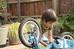 Boy in garden repairing upside down bicycle looking down