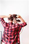 Young man looking in mirror, putting hair in ponytail, rear view