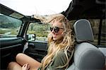 Young woman with windswept long blond hair on the road in jeep