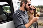 Young couple leaning against jeep eating ice cream cones