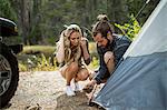 Young couple putting up tent on forest riverside, Lake Tahoe, Nevada, USA