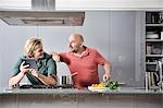 Male couple looking at digital tablet whilst preparing food in kitchen