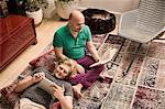 Male couple on living room floor reading book and digital tablet