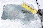 Hand clearing snow from windshield, woman on background