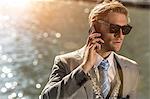 Young businessman wearing sunglasses talking on smartphone on waterfront