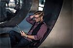 Young businessman reclining on curved wall reading digital tablet