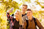 Young woman taking selfie with two teenage brothers in autumn forest