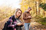 Teenage boy and adult sister reading smartphone texts in autumn forest