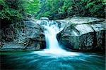 Large rain forest waterfall, sun beams, and mossy rocks